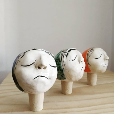 Três rolhas decorativas de cerâmica com faces femininas e diferentes cores de cabelo.
