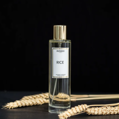 Frasco transparente de perfume com tampa dourada e etiqueta METORICE RICE junto a espigas de cereal