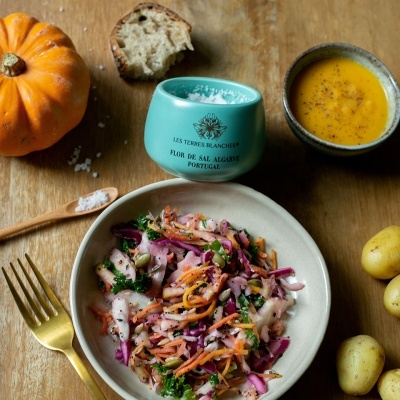 Salada de legumes num prato cerâmico com sopa, salgadeira azul, pão, abóbora e batatas numa mesa de madeira