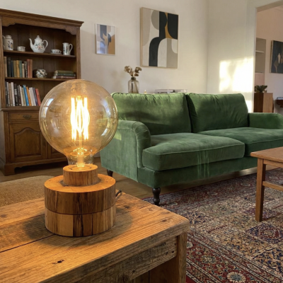 Lâmpada de madeira e vidro com filamento numa sala com sofá verde e estante de madeira
