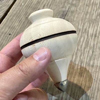 Peão de madeira clara com ponta metálica e aro preto