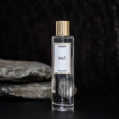 Frasco de vidro com líquido e tampa dourada com etiqueta MEMORICE SALT sobre superfície preta e pedra cinza