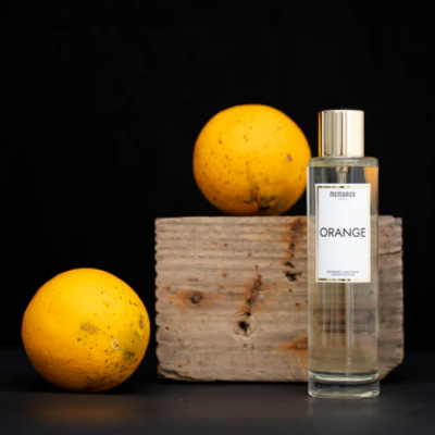 Frasco de perfume MEMORICE ORANGE ao lado de duas laranjas e bloco de madeira