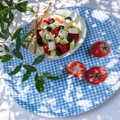 salada de queijo feta com tomate, azeitonas e pepino num prato branco sobre toalha azul clara xadrez