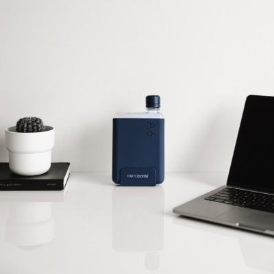 Garrafa de água azul escuro com texto A6 e memobottle numa secretária com cacto e laptop