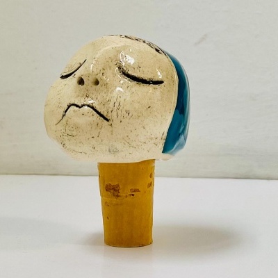 Rolha de cortiça com cabeça cerâmica pintada em bege e azul com expressão triste