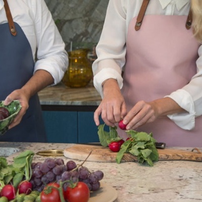 Duas pessoas com aventais preparam legumes frescos numa bancada de cozinha