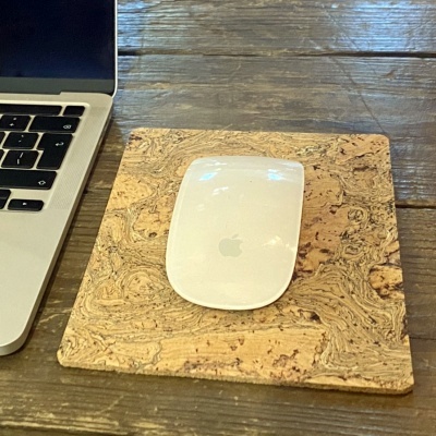 Rato Apple branco sobre suporte de cortiça quadrado em mesa de madeira com teclado de portátil