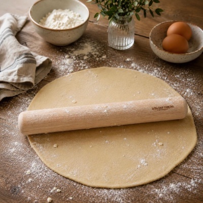 Rolo de massa de madeira numa mesa com massa estendida e ingredientes para cozedura