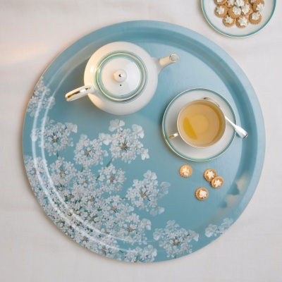 Tabuleiro azul redondo com flores brancas, chávena de chá, bule branco e biscoitos