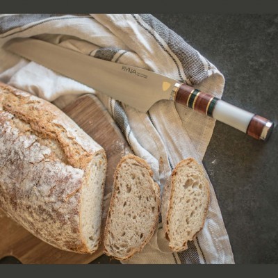 Faca de corte de aço inoxidável com cabo em madeira e metal ao lado de pão rústico cortado sobre pano e superfície escura
