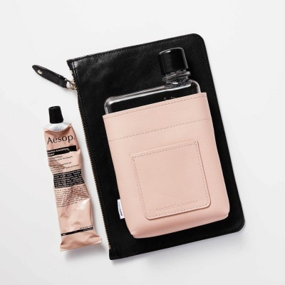 Bolsa preta, garrafa em suporte rosa e creme Aesop