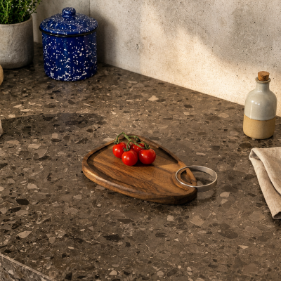 Bancada de cozinha em pedra castanha com tábua de madeira, tomate-cereja, frascos cerâmicos e vaso com planta