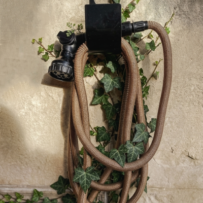Mangueira de jardim castanha com suporte preto e folhas verdes de hera na parede de pedra.