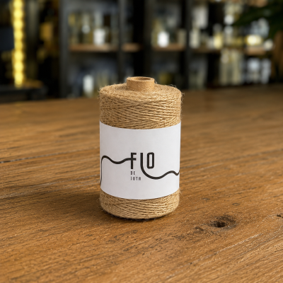 Rolo de fio de juta com etiqueta FLO DE JUTA sobre mesa de madeira.
