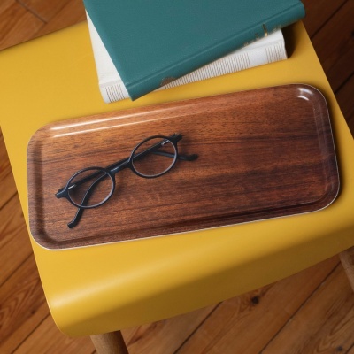 Bandeja de madeira com óculos pretos numa mesa amarela com livros