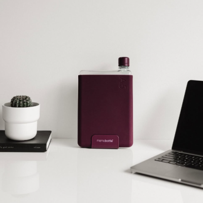 Garrafas de água Memobottle com capa vinho ao lado de cacto e portátil numa mesa branca