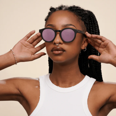 Óculos de sol com armação preta e lentes rosa espelhadas num modelo com cabelo trançado.