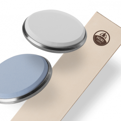 Dois relógios de mostrador branco e azul sobre superfície preta ao lado de embalagem bege com logótipo HORI