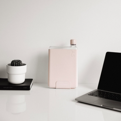 Garrafa de água cor-de-rosa A5, computador portátil e cacto numa mesa branca