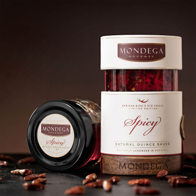 Frascos de molho natural de marmelo picante da marca MONDEGA sobre superfície escura com especiarias.