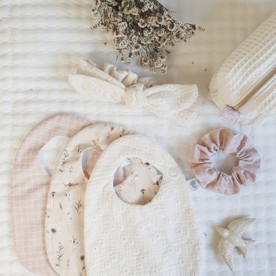 Babetes de bebé, elástico e faixa de cabelo, pomba decorativa e raminho seco sobre manta branca.