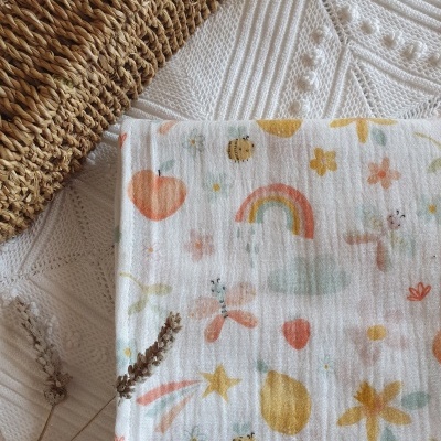 pano branco com padrão colorido de arco-íris, estrelas, abelhas e frutas sobre superfície branca texturada