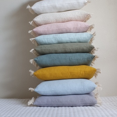 Pilha de almofadas coloridas em tecido waffle contra parede branca.