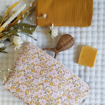 Necessaire floral, toalha castanho-alaranjada, escova de madeira, barra de sabão amarelo e flores secas sobre fundo branco acolchoado