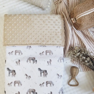 Produtos de bebé com manta de cavalos, toalhas bege, necessaire castanha, pano riscado, flores secas e massageador de madeira