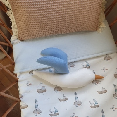 Berço com roupa de cama de faróis e barcos, almofada rosa e peluche de gaivota