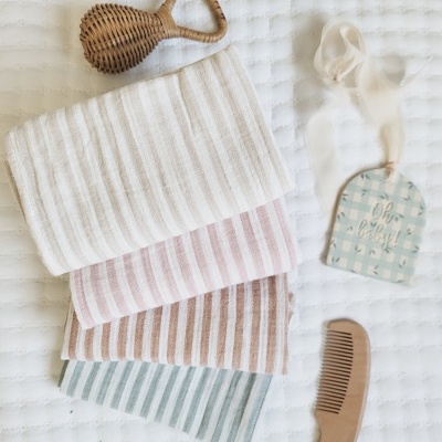 Toalhas às riscas, pente de madeira e etiqueta com texto 'Oh so cute!' sobre superfície acolchoada branca