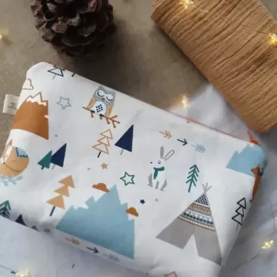 Necessaire com padrão infantil de animais e montanhas sobre fundo bege com rolo de tecido castanho e pinheiro seco