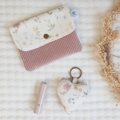 bolsa rosa com aba branca floral, chaveiro coração floral e batom rosa claro sobre tecido branco texturado