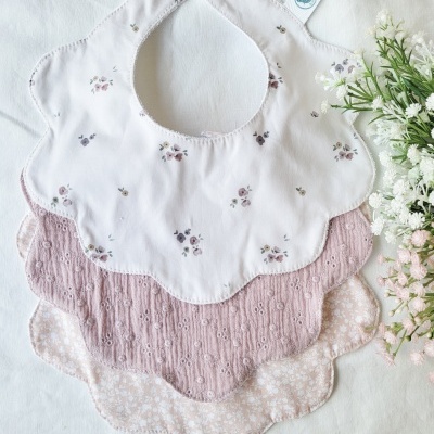 Três babetes florais para bebé com bainhas onduladas sobre tecido branco