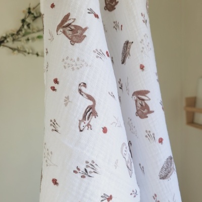 Fralda branca com desenhos de coelhos, esquilos e ouriços em tons castanhos e vermelhos