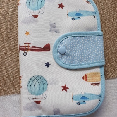 Estojo branco com padrões de balões e aviões coloridos e fecho azul com pontos brancos