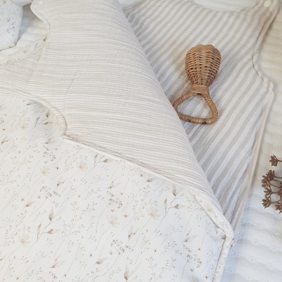 Cobertor branco com padrões florais e riscas numa cama com chocalho de vime.