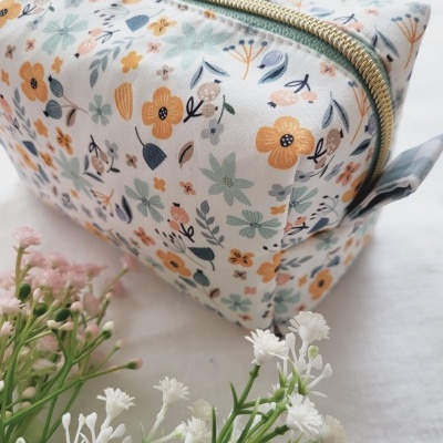 Necessaire retangular com padrão floral em tons suaves e fecho dourado sobre fundo branco com flores