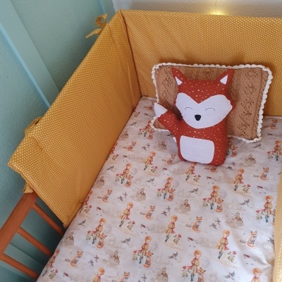Berço de madeira com protetores amarelos, lençol estampado e pelúcia de raposa
