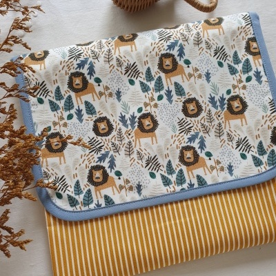 Manta infantil com padrão de leões, tecido riscado amarelo e branco, objeto de vime ao lado