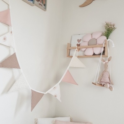 Quarto infantil decorado com almofadas, varal de bandeirolas de tecido, prateleira com almofada flor e brinquedo de peluche em baloiço de madeira