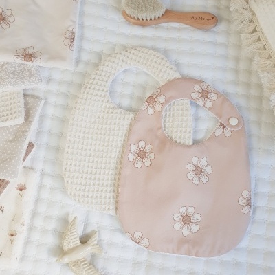 Babete rosa com flores, babete branco, pente em madeira e pano com flores sobre manta branca