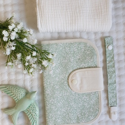 Conjunto de acessórios para bebé com padrão floral verde claro e branco, sobre fundo branco texturizado.