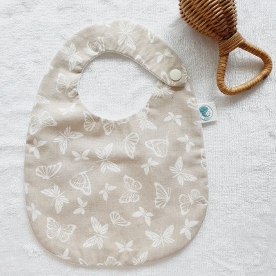 Babete bege com padrão de borboletas brancas e chocalho de palha