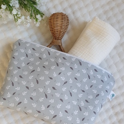 Bolsa azul com padrão de folhas, colher de madeira, tecido branco e flores ao lado