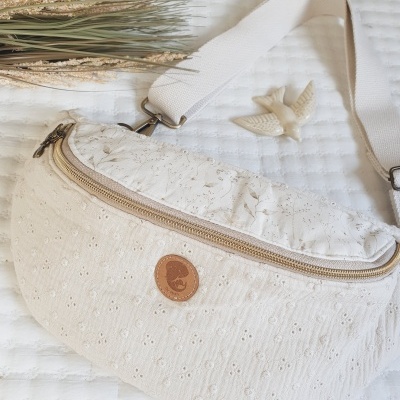 Pochete branca com padrão bordado, alça larga e selo de couro, com decoração natural e figura de pássaro em fundo branco.