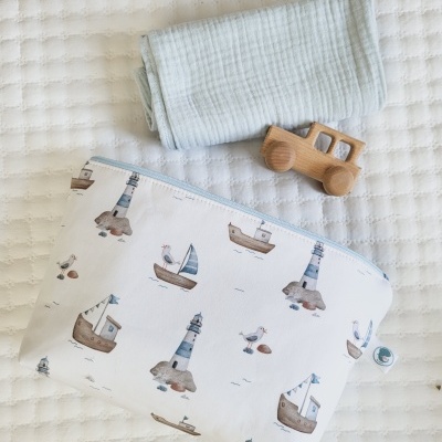 Mala com padrão náutico, muselina azul claro e brinquedo de madeira sobre tecido branco