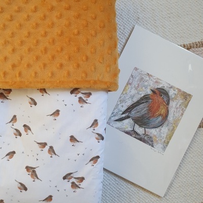 Manta mostarda com relevo e tecido branco com padrão de pássaros sobre tapete branco com bordas bege, e ilustração de pássaro em papel