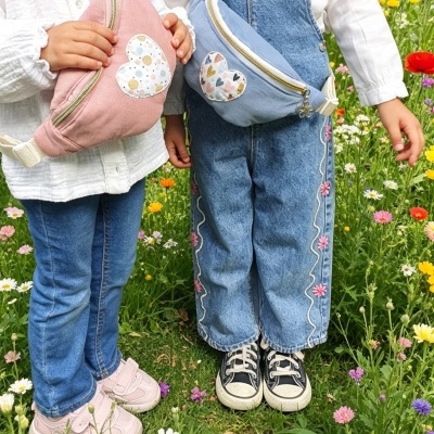 Duas raparigas segurando pochetes cor-de-rosa e azul com corações estampados em campo florido.